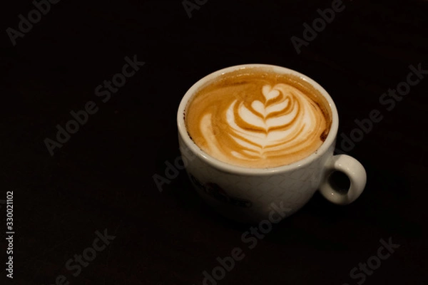 Fototapeta A cup of cappuccino with a flower in the milk foam on black background - latte art coffee shop concept
