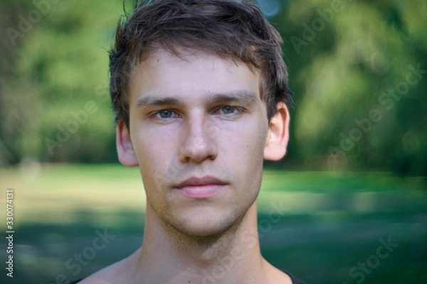 Fototapeta Portrait of relaxed a young man standing in a park with a plane and honest look on his face on a summer afternoon.