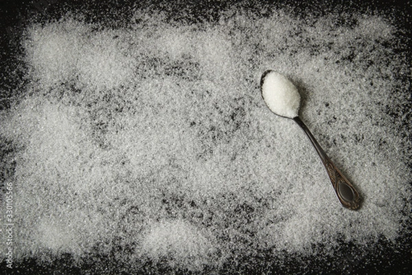 Obraz white sugar on a black background with a spoon of sugar