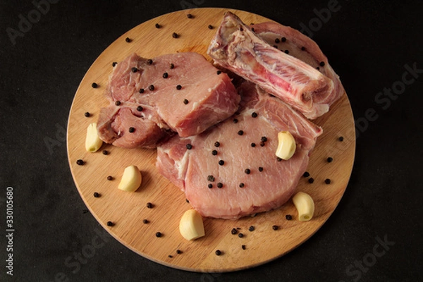 Obraz meat, raw steaks with garlic and pepper on a wooden board, black background
