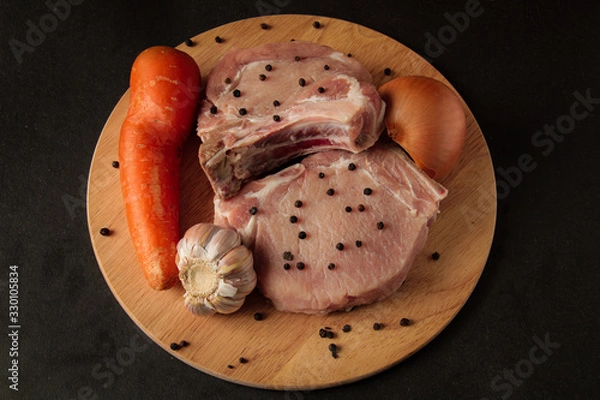 Obraz two steaks, raw meat, with vegetables, onions garlic, carrots and peppers, on a wooden board