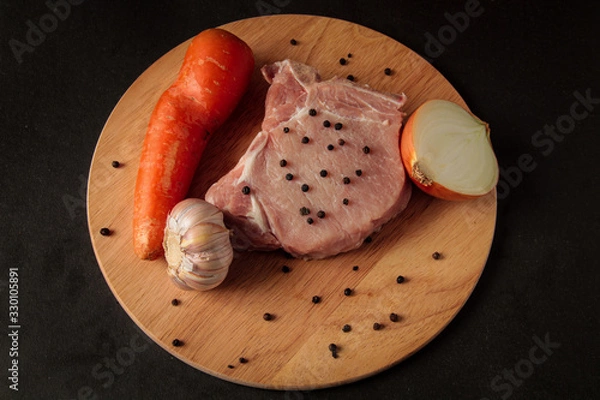 Obraz one raw meat steak, on a wooden board, sprinkled with pepper, with vegetables, onions, garlic, carrots