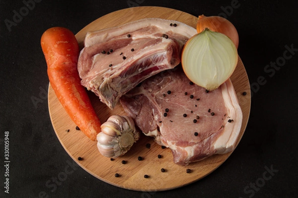 Obraz slices of strictly pork steak with vegetables, peppers, carrots, chopped onions, on a wooden board and black background