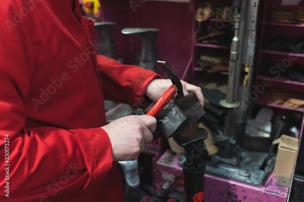 Fototapeta Detail of a shoemaker's hands dressed in red working with a hammer and shoes