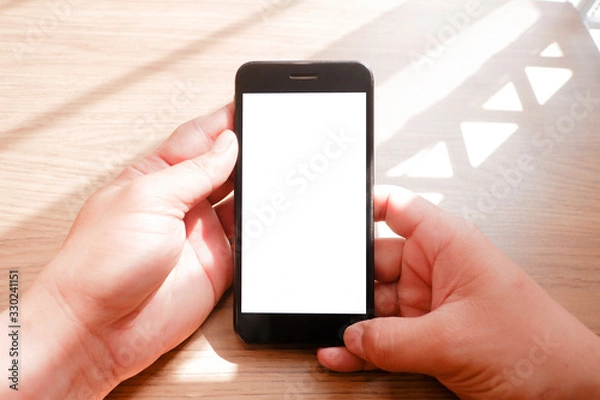 Fototapeta Mockup picture of business man’s hands holding smart phone with white blank screen in modern place