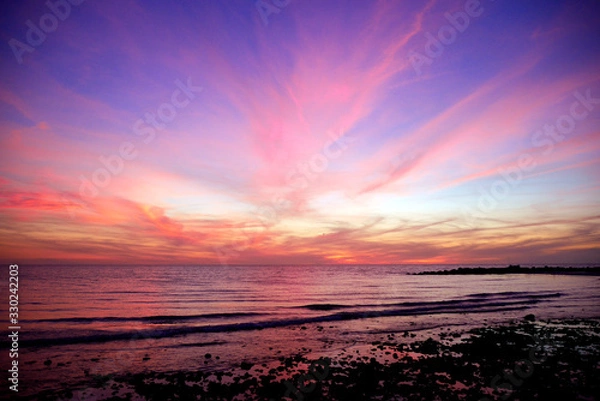 Obraz Clouds radiate red like fireworks against a purple sky from the post glow of a sunset, mirrored I the calm waters of the Gulf of Mexico on the west coast of Florida.