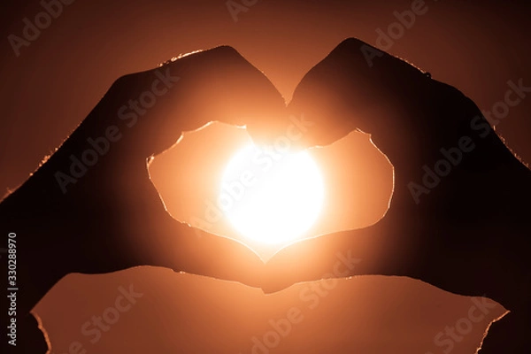 Obraz Female hands in heart shape in focus holding sun circle inside