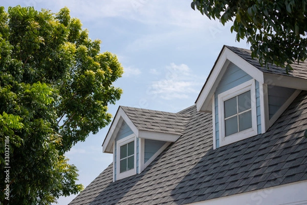 Fototapeta Roof shingles with garret house on top of the house among a lot of trees. dark asphalt tiles on the roof background