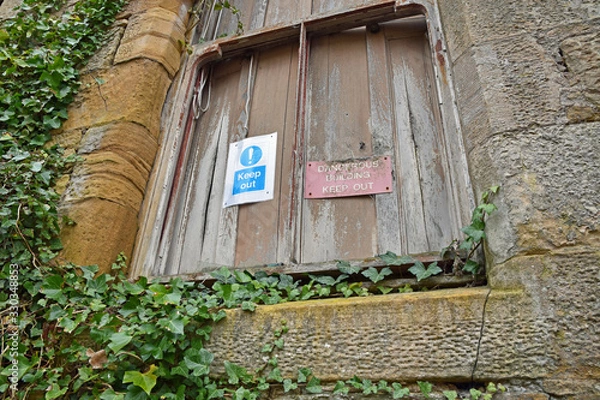 Fototapeta Keep out dangerous building signs on boarded up window with climbing ivy surrounding. Crawford Priory, Cupar, Fife, Scotland: an abandoned, derelict gothic mansion.