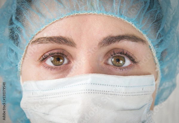 Fototapeta Nurse in a white mask. The face is close. Tired sad eyes of a paramedic after a hard day's work.  slanting eyes.  coronavirus