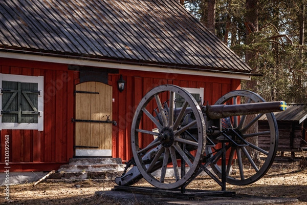 Fototapeta An old cannon next to a historic house in the woods