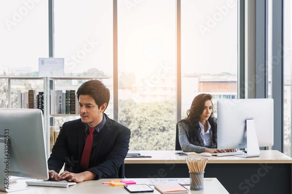 Obraz Concentrated asian businessman and caucasian business woman using computers in modern office, working separately on project.