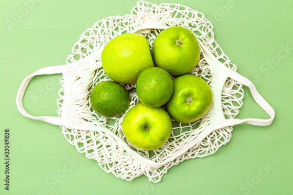 Fototapeta Net bag with green fruits on a green background. Zero waste. Monochrome green.