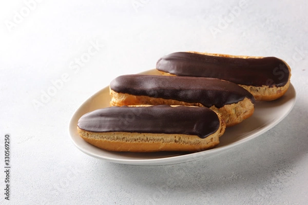 Fototapeta Dessert. Eclairs with chocolate glaze. Cake with cream on the white plate on a light background. Background image, copy space