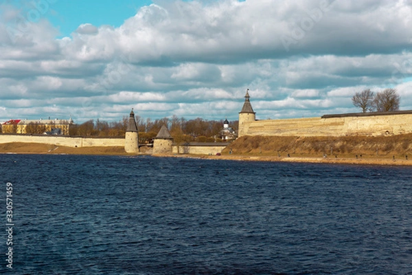 Fototapeta Spring panorama of an old medieval fortress standing on the river Bank. Pskov, Russia.