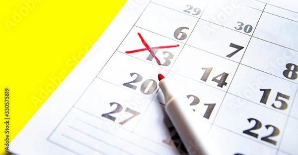 Fototapeta Numbers on the calendar crossed out with a red cross in macro on a yellow background. Calendar for plans, notes, meetings. Business calendar.  Marker for notes on the calendar. In the foreground.