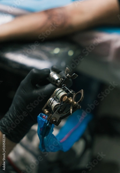 Obraz A selective focus shot of a hand of a tattoo artist wearing a black glove and holding a tattoogun