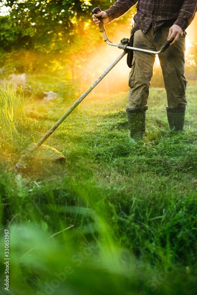 Fototapeta Man mowing the grass with trimmer