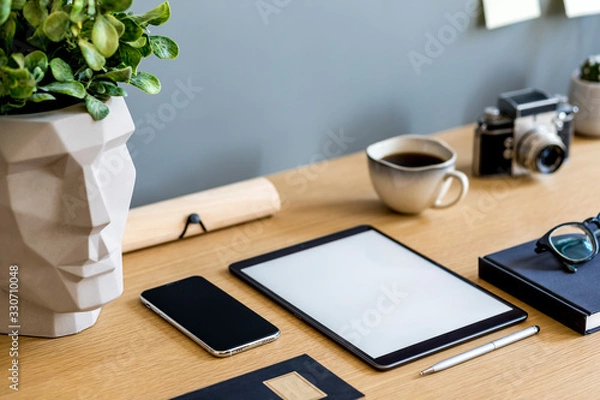Fototapeta Modern business composition on the wooden desk with mock up tablet screen, plant, photo camera, notes, mobile phone and office supplies in stylish concept of home decor.