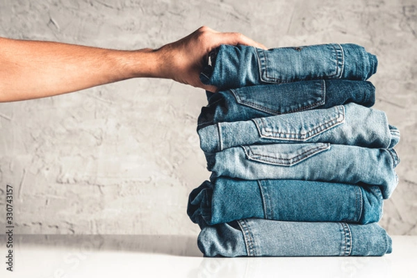 Fototapeta Hands, put the stack of blue jeans on gray background.