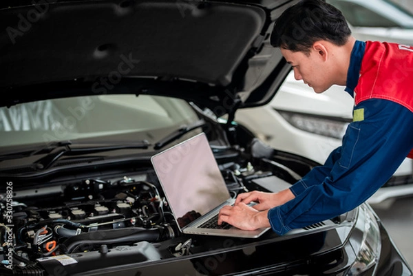 Fototapeta Technicians check and fix cars in the garage The technicians in the auto repair shop use computer systems to check engine problems - car repair services, maintenance concepts.