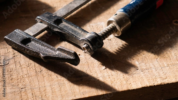 Fototapeta Clamp tool on a wooden background.  F-clamp, bar clamp, speed clamp and a G-clamp.