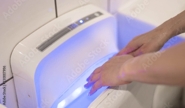 Fototapeta Female wet hand in modern vertical hand dryer in public restroom.