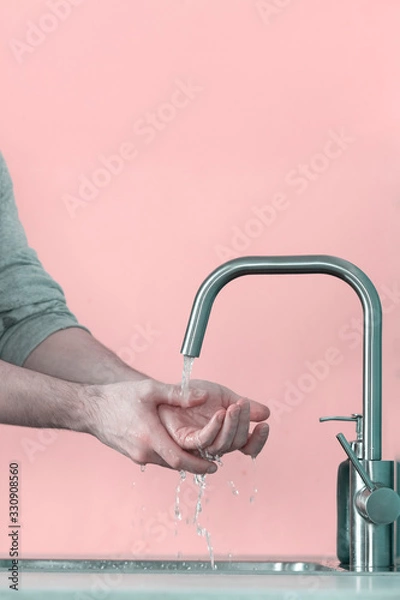 Fototapeta One young man washes his hands - before eating or after eating closeup in the kitchen against pink wall background