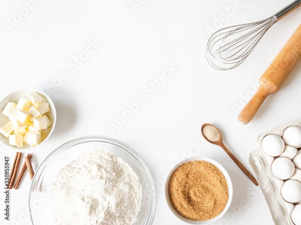 Fototapeta Frame of various baking ingredients - flour, eggs, sugar, butter, dry yeast, nuts and kitchen utensils on white background. Top view.