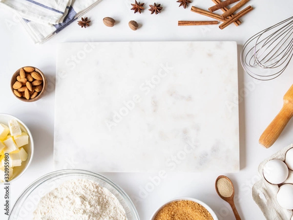 Fototapeta Frame of various baking ingredients - flour, eggs, sugar, butter, dry yeast, nuts and nuts, kitchen utensils and white marble board. Top view.