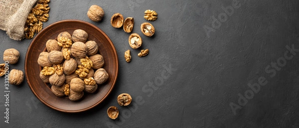 Fototapeta Nuts. Walnut kernels and whole walnuts on dark stone table. Black background. Top view, flat lay with copy space.