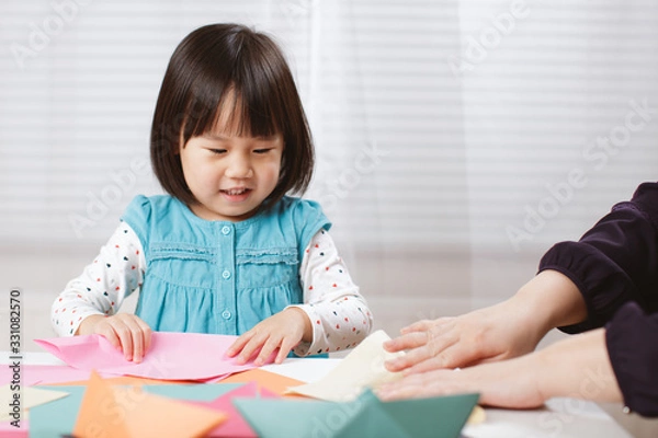 Fototapeta toddler girl learn making  Origami at home against white background