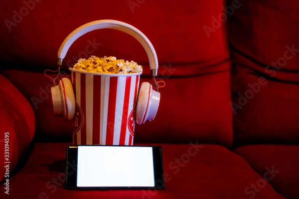 Obraz mobile phone with empty white bright screen with popcorn bucket on the red sofa. Concept of streaming TV on internet phone.