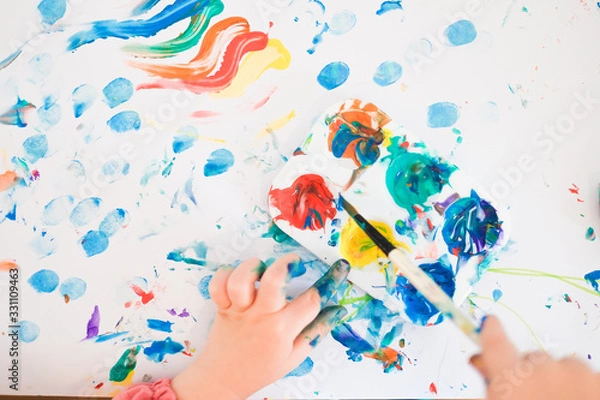 Fototapeta A child is painting with fingers and brush and oil paints