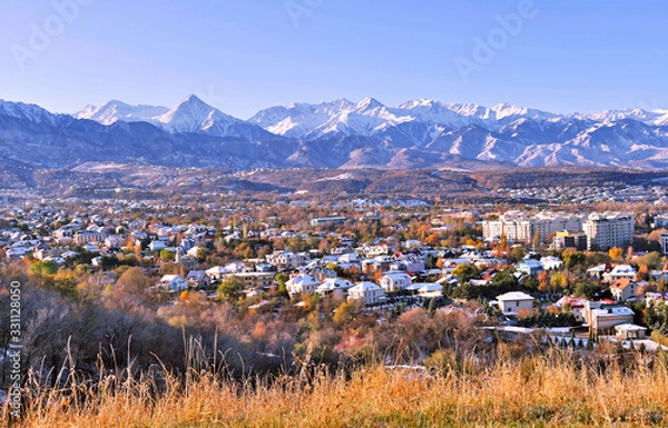 Fototapeta Upper part of Almaty city on the background of mountains in autumn season; first snow on the roofs of houses in golden fall, beauty and greatness of Kazakhstan concept