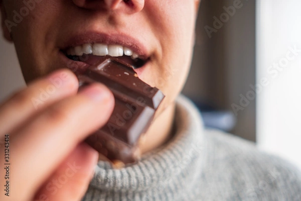 Obraz a person enjoying a piece of chocolate with hazelnuts. Eating chocolate and holding it with her hand.