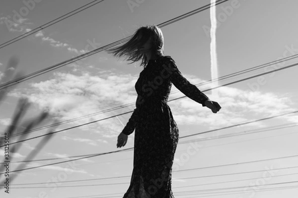 Fototapeta Beautiful girl in a dress in the countryside. Against the background of a field and high-voltage wires among wheat. Blue sky and model