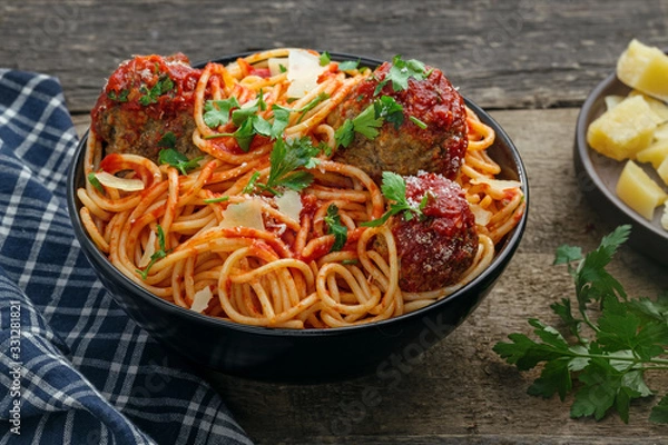 Obraz Pasta with meatballs, parmesan and tomato sauce in a clay bowl. Homemade Italian spaghetti on a rustic wooden table.