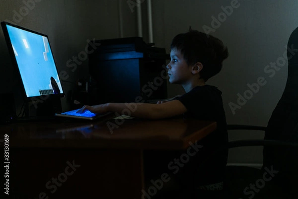 Fototapeta child boy plays computer games in a dark room