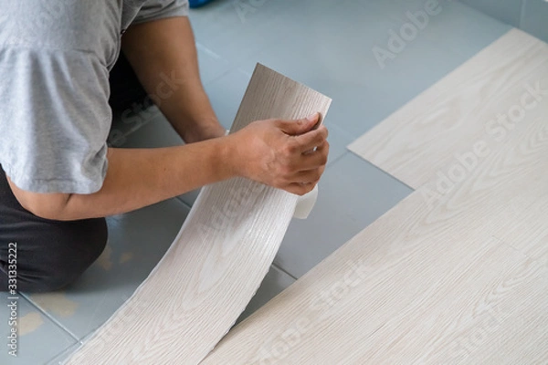 Fototapeta A person installing new vinyl tile floor, a DIY home project.