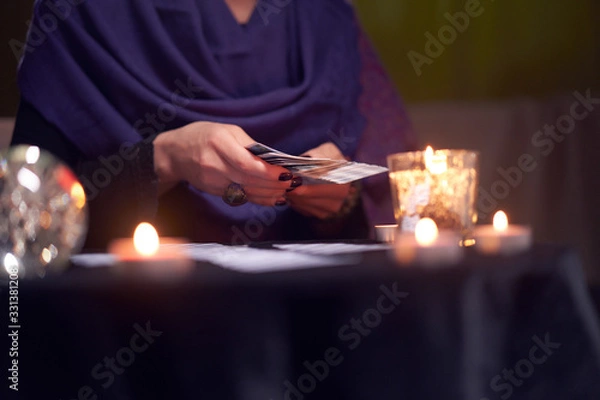 Fototapeta Close-up of fortune teller female divining on cards sitting at table with burning candles, magic ball