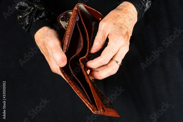 Fototapeta Empty shabby wallet in hands of old poor lady. Concept of a lack of money in old age and small pensions. Close-up in dark key.