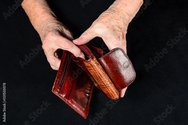 Fototapeta Elderly woman holds an empty old wallet in her hands. Concept of lack money in old age and small pensions. Close-up in dark key.