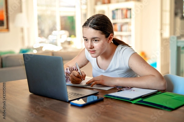Fototapeta Nastolatka studiuje online w domu, patrząc na laptopa w okresie kwarantanny podczas pandemii. Nauka w domu. Dystans społeczny. Test szkolny online.