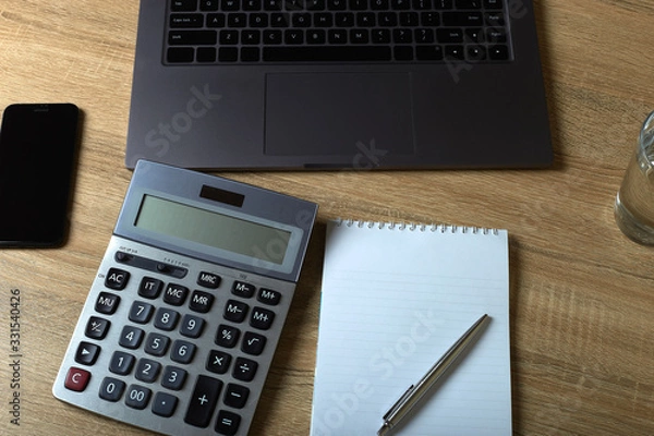Fototapeta Remote work laptop calculator notepad with pen and glass of water on the table