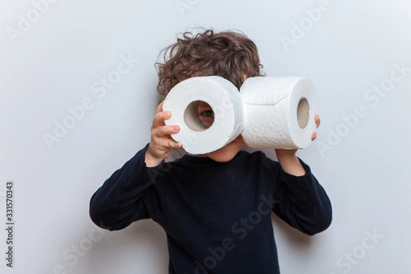 Fototapeta a little boy a child holds two rolls of toilet paper in his hands depicting binoculars or glasses.