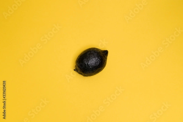 Fototapeta Black lemon on the yellow background. Minimal style. Top view. The lemon at the centre of the frame. Minimal art. Fruit. One