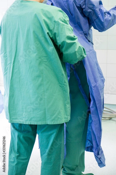 Fototapeta OP Saal in einem Krankenhaus, ein Pfleger zieht dem Arzt einen sterilen Kittel an