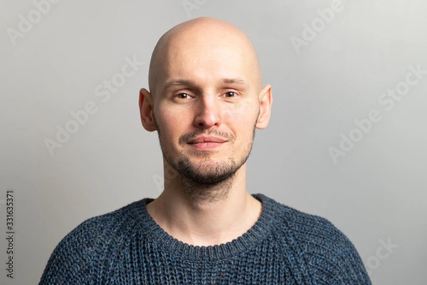 Obraz portrait of a young bald man in a knitted sweater on a gray background