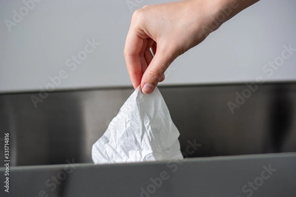 Fototapeta Women hand throwing a white used crumpled tissue paper into a garbage trash bin.